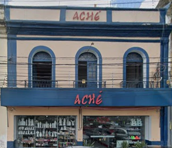 Fachada da Aché: casarão azul e bege com três arcos e o letreiro vermelho